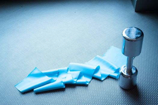 Silver dumbbell next to elastic band for pilates exercises. No people