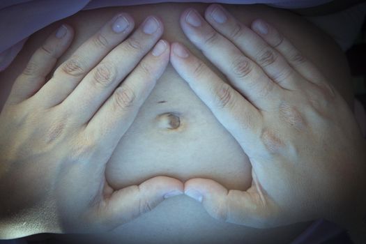 Gut of seven months pregnant woman making a heart with her hands. Peace scene