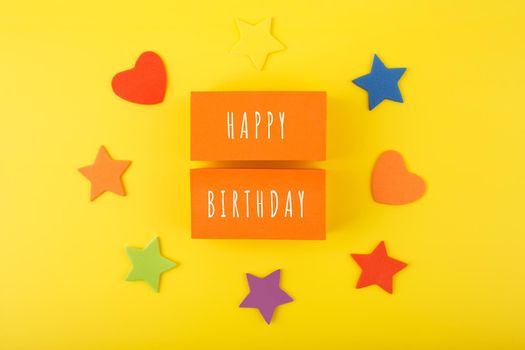 Happy Birthday bright fun colorful concept on yellow background decorated with hearts and stars. Happy Birthday written on orange tablets against yellow background