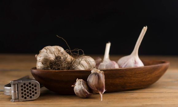 Organic garlic with metal press. Fresh garlic cloves and garlic bulb on a wooden table. Garlic for healthy eating. Concept of spices for healthy cooking. Closeup
