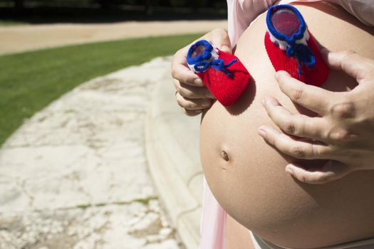 Seven months pregnant woman with red and blue booties on her belly