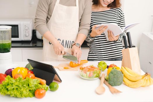 Happy couple in kitchen together. Man cutting vegetables and making salad while his wife reading recipe