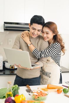 Asian woman showing something on the laptop to her boyfriend in the kitchen
