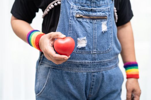 Asian lady wearing rainbow flag wristbands and hold red heart, symbol of LGBT pride month celebrate annual in June social of gay, lesbian, bisexual, transgender, human rights.