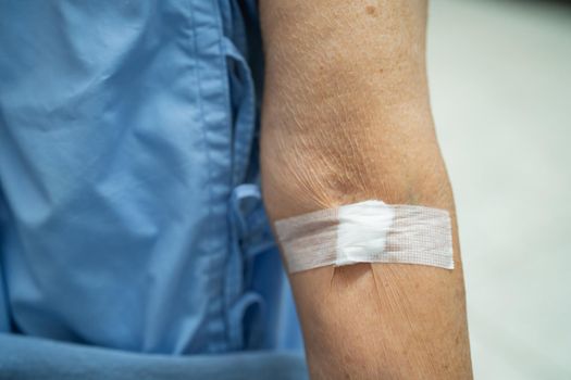 Asian senior or elderly old lady woman patient show cotton wool stop bleeding, after blood drawing testing for annually physical health check up to check cholesterol, blood pressure, and sugar level.