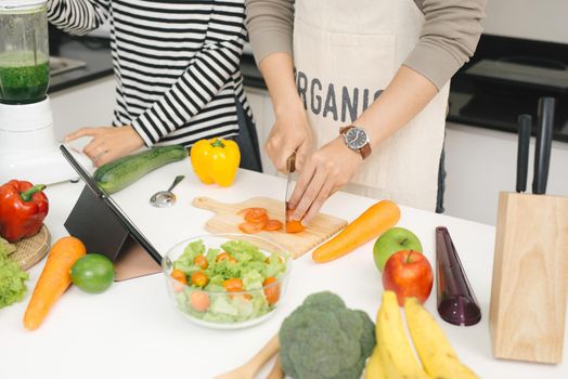 Cooking on family kitchen. Young and beautiful loving couple cooking and help each other while preparing dinner with vegetables