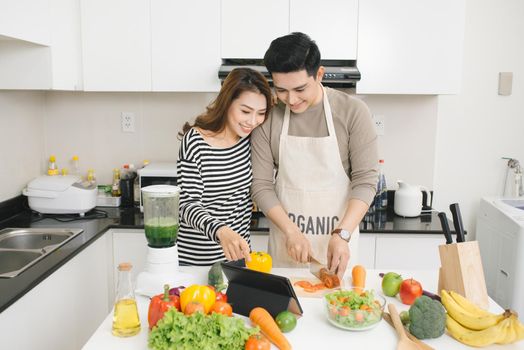 Young asian couple chopping vegetable and using digital tablet in the kitchen