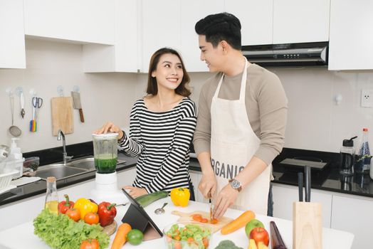 Happy asian couple have fun in modern kitchen indoor while preparing fresh fruits and vegetables food salad