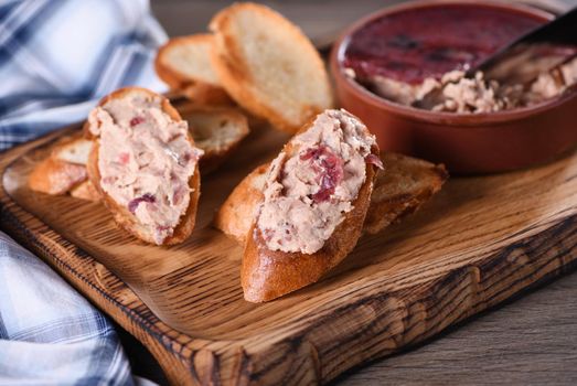 Delicate chicken pate with mashed cranberries spread on toasted baguette slices. Country style food.