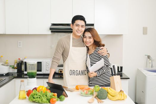 Happy asian couple following recipe on digital tablet when cooking