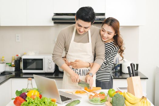 Happy asian couple watching tv show on the laptop and cooking dinner