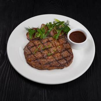 Grilled black angus steak ribeye on white plate on black wooden background