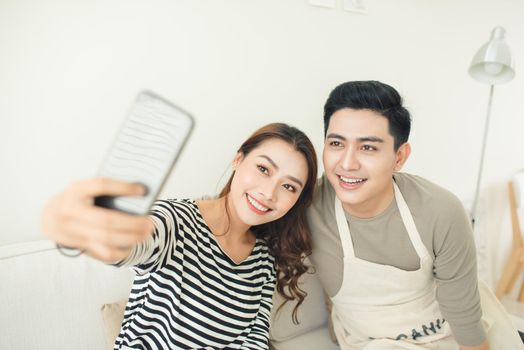 Portrait of a smiling couple making selfie photo on smartphone at the kitchen