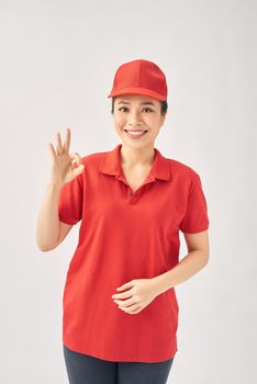 Happy young girl courier, wearing cap uniform looking at camera showing ok sign recommend fast delivery service on white background.