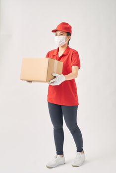 A uniformed courier wearing medical rubber gloves and a medical mask holds a paper box of food on a white background. 