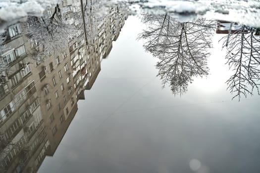 Reflection on the puddle of winter snow covered city scenery.