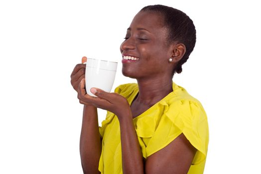 young girl standing in yellow tank top approaching a cup towards the mouth smiling with closed eyes.