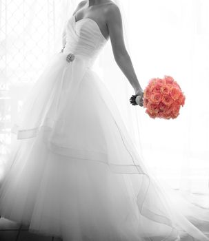 Softly focused monotone bridal image in window light with colorized rose bouquet