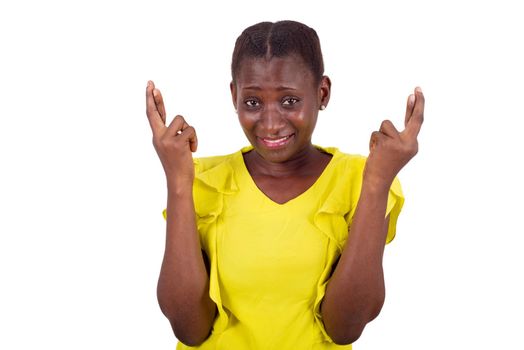 young girl standing in yellow camisole looks at the camera smiling with crossed fingers