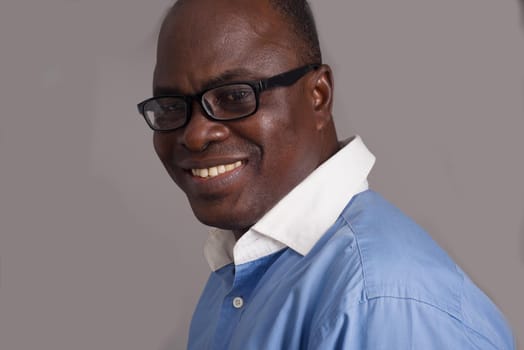 african adult man in blue shirt in glasses looking at camera smiling on gray background.