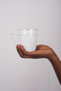 a white cup placed in a feminine palm on a gray background.