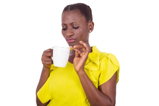 young girl standing in yellow camisole staring into a cup she has in her hand.