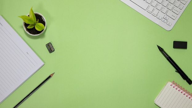 Flat lay black to school and education concept on green background with blank notepad, keyboard , green plant and supplies.