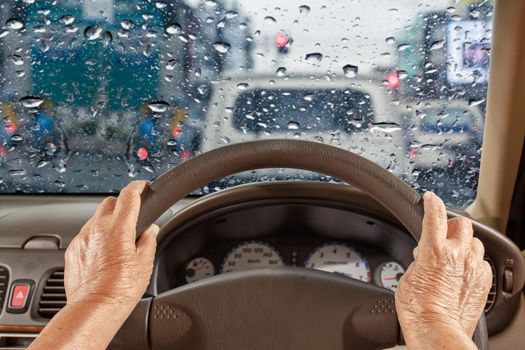 Senior woman driving a car slowly in city ,rainy season
