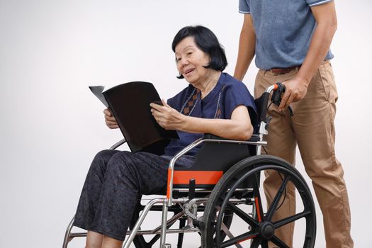 elderly woman reading a book on wheelchair with her son take care.