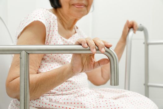 Elderly woman holding on handrail in toilet.