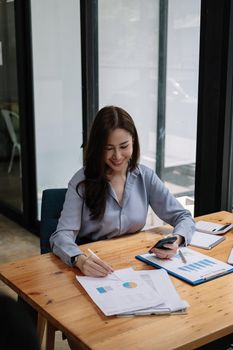 Business asian woman using smartphone for do math finance on wooden desk in office, tax, accounting, financial concept.