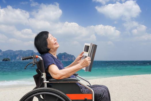 Senior asian woman laughing while reading magazine on beach