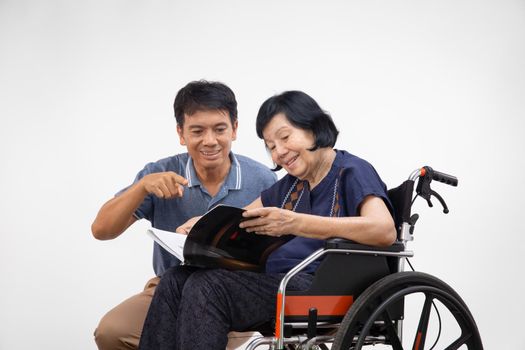 Elderly woman reading a book on wheelchair with her son take care.