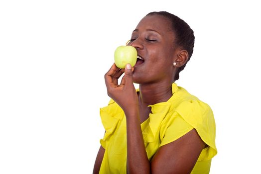 young girl standing in yellow camisole holding an apple on her mouth with her eyes closed.