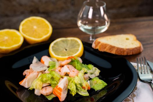 composition of a black plate with shrimp and surimi salad on wooden background