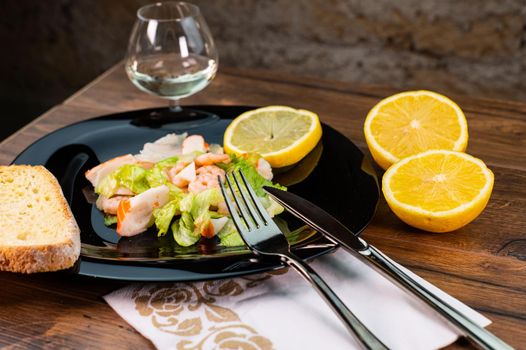 seafood salad composition with shrimps and surimi with cutlery and glass of white wine and lemons