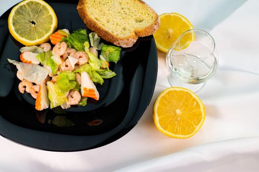 composition of a black plate with shrimp and surimi salad on a white satin background