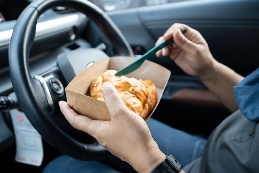 Asian lady holding ice coffee and bread bakery in car dangerous and risk an accident.