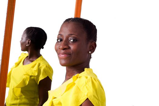 African girl standing in yellow tank top in front of a mirror and looking at camera smiling.