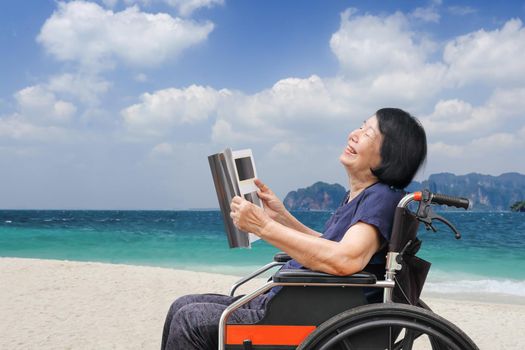 Senior asian woman laughing while reading magazine on beach