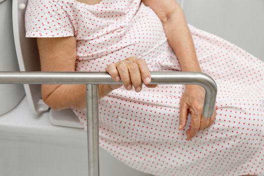 Elderly woman holding on handrail in toilet.