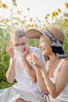 Autumn nature. Fun and liesure. Young teenage couple having picnic on sunflower field in sunset, having fun looking away, wiping their hands and faces