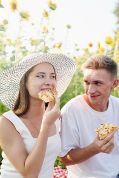Young teenage couple picnic on sunflower field in sunset. Eating pizza and drinking champagne