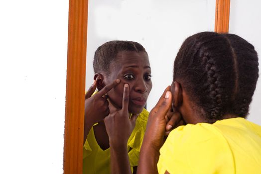 African girl standing in yellow camisole looking at herself in a mirror.
