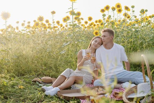 Autumn nature. Fun and liesure. Young teenage couple having picnic on sunflower field in sunset drinking champagne