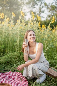 Autumn nature. Fun and liesure. Young teenage girl having picnic on sunflower field in sunset drinking champagne