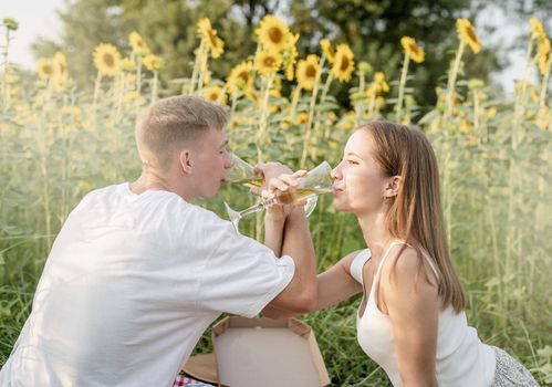 Autumn nature. Fun and liesure. Young teenage couple picnic on sunflower field in sunset drinking champagne toasting