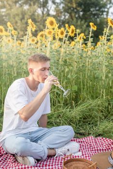 Autumn nature. Fun and liesure. Young teenage boy having picnic on sunflower field in sunset drinking champagne