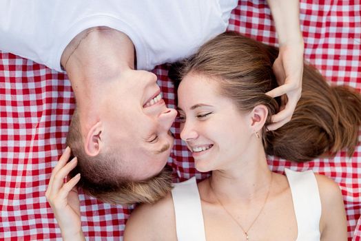 Young happy romantic couple cuddling on a picnic blanket looking to each other, top view