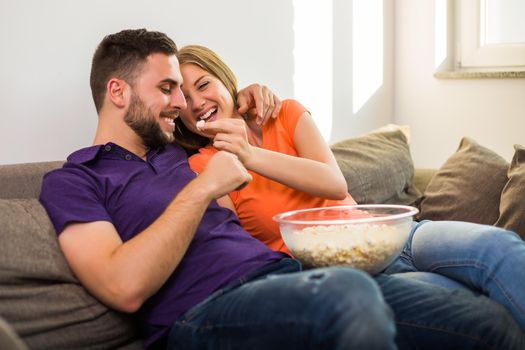 Couple in love eating popcorn and having fun while they enjoy spending time together at their home.